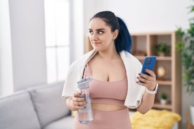 Young caucasian woman smiling confident holding water using smartphone at home