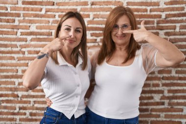 Latin kökenli anne ve kız günlük beyaz tişörtler giyip el ve burun parmaklarını göstererek neşeli bir şekilde gülümsüyorlar. güzellik konsepti 