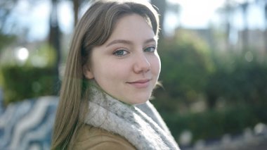 Parkta kendinden emin gülümseyen genç sarışın kadın.