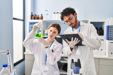 Erkek ve kadın bilim adamı partnerler laboratuardaki panoda test tüpü yazıları tutuyor.