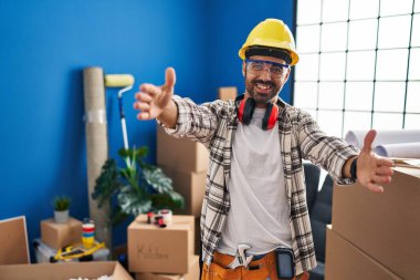 Evde tadilat yapan sakallı genç İspanyol adam kameraya sarılıp gülümsüyor. Mutluluğu kucaklayan neşeli bir ifade.. 