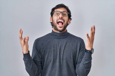 Tecrit edilmiş arka planda duran yakışıklı Latin adam başarı için deli ve çılgınlığı kutluyor kollarını kaldırmış ve gözlerini kapatmış heyecanla bağırıyor. Kazanan konsept 