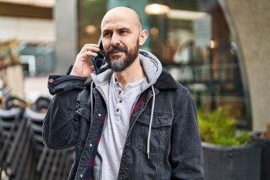 Genç kel adam gülümsüyor. Kendine güveni tam. Akıllı telefondan konuşuyor.