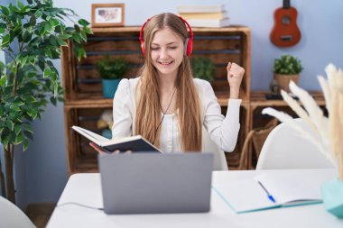 Bilgisayar laptopuyla çalışan beyaz bir kadın gururla bağırıyor, zaferi kutluyor ve kollarını kaldırdığı için heyecanlanıyor. 