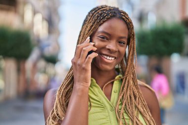 Afro-Amerikalı kadın gülümsüyor. Akıllı telefondan konuşuyor.
