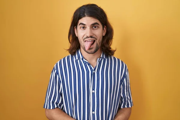 長い髪を持つヒスパニック系の男は面白い表現で幸せ舌を突き出して黄色の背景に立っている 感情の概念 — ストック写真