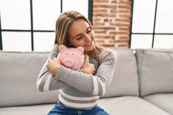 Young Blonde Woman Smiling Confident Hugging Piggy Bank Home — 스톡 사진