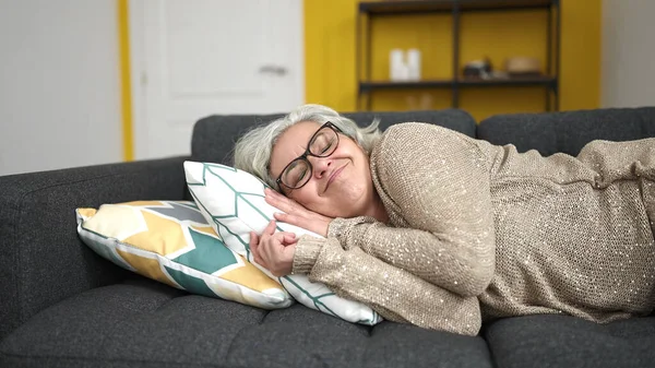 Middle age woman with grey hair lying on sofa sleeping at home