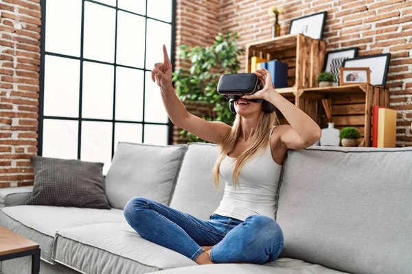 年轻的金发女人在家里用虚拟现实眼镜玩电子游戏 — 图库照片