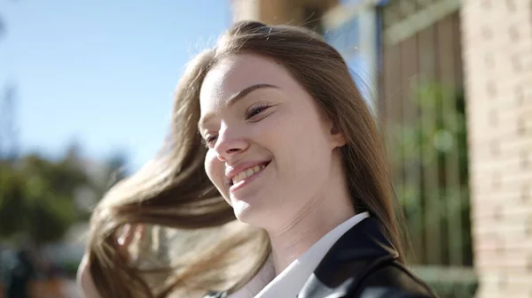 年轻的金发女人带着自信的笑容在街上梳理着头发 — 图库照片