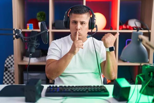 若いヒスパニック系の男がビデオゲームをプレイする側に手を指して唇に指で静かにするように求めている 沈黙と秘密の概念 — ストック写真
