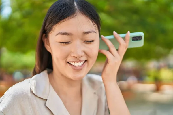 中国人女性の笑顔自信を持ってリスニング音声メッセージによるスマートフォンによって公園 — ストック写真