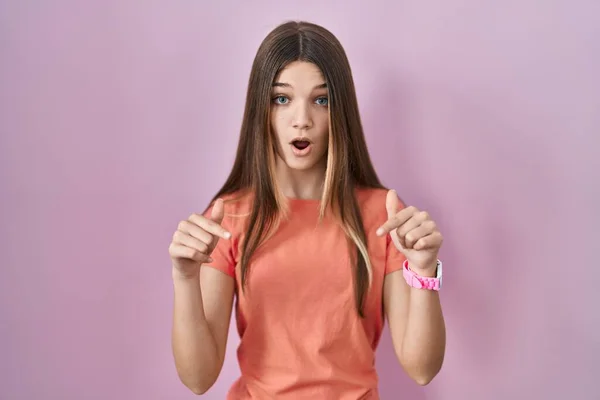 少女站在粉红的背景上 手指垂下 展示广告 惊讶的脸和张开的嘴 — 图库照片