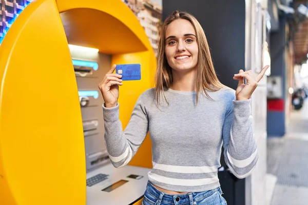 年轻的医生女士拿着信用卡在现金点上开心地微笑着 手指头指向旁边 — 图库照片