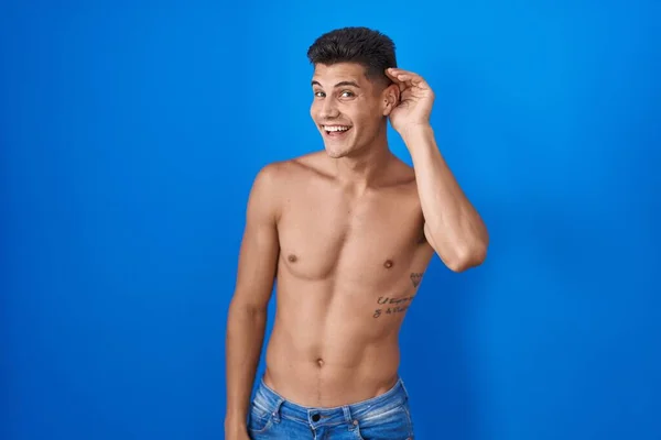 Mavi Arka Planda Tişörtsüz Dikilen Genç Spanyol Adam Kulağına Fısıldayarak — Stok fotoğraf