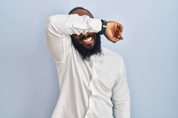 アフリカ系アメリカ人の男性が青い背景に腕を笑顔で陽気で面白い目をカバー立っている 視覚障害の概念 — ストック写真