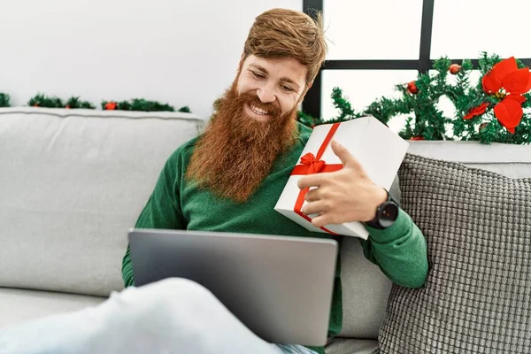 年轻的红头发男人坐在家里的圣诞装饰旁边 用笔记本电脑 — 图库照片