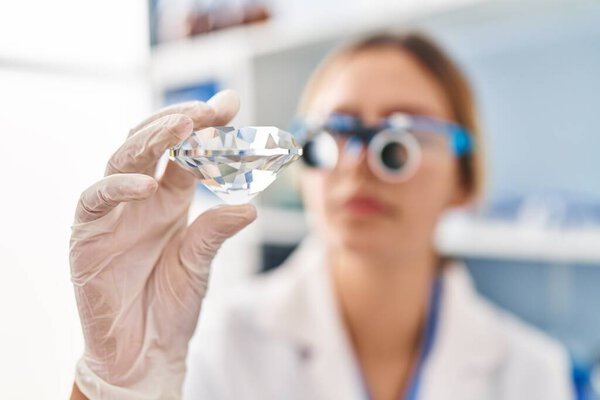 Young hispanic woman scientist looking diamond with zoom glasses at laboratory