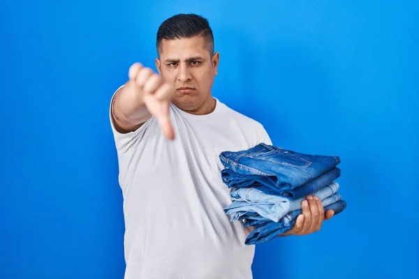 Jovem Hispânico Segurando Pilha Jeans Dobrados Com Rosto Irritado Sinal — Fotografia de Stock