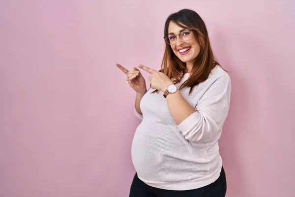 Mujer Embarazada Pie Sobre Fondo Rosa Sonriendo Mirando Cámara Apuntando —  Fotos de Stock