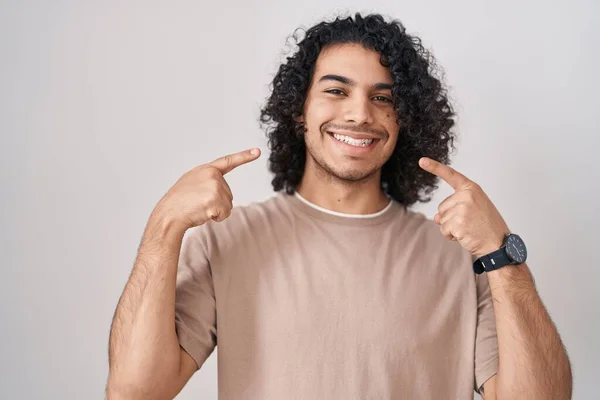 头发卷曲的西班牙裔男子站在白色的背景上 笑容满面 用手指和嘴指尖 牙齿健康概念 — 图库照片