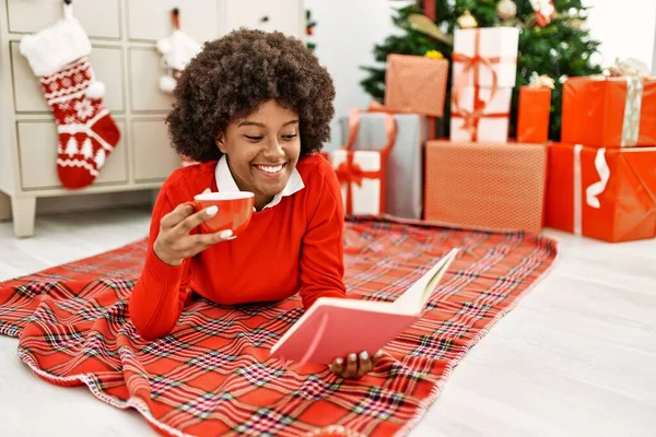 若いですアフリカ系アメリカ人女性飲料コーヒーと読書本横にクリスマスツリーにホーム — ストック写真