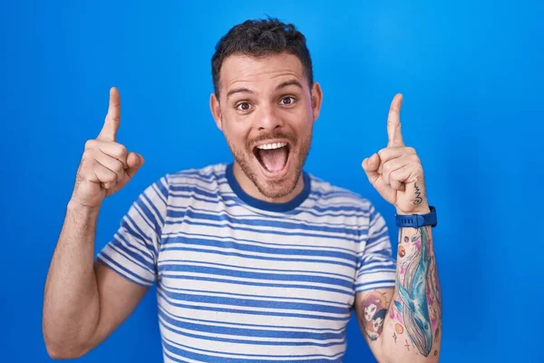 Young Hispanic Man Standing Blue Background Smiling Amazed Surprised Pointing — Stock Photo, Image