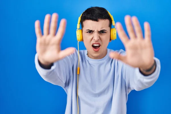 使用耳机听音乐的非二进制人 用手掌 愤怒和沮丧的表情做停止手势 — 图库照片