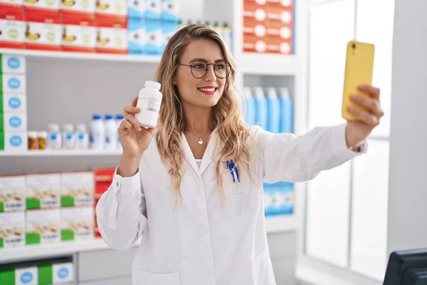 年轻的女药剂师在药店拿着药瓶用智能手机自制药物 — 图库照片