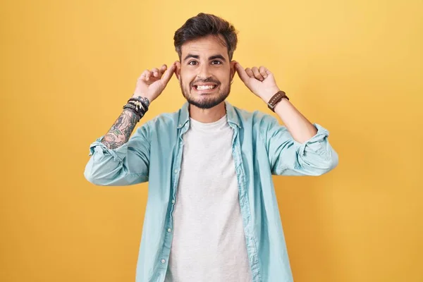 Молодий Іспаномовний Чоловік Татуюваннями Стоїть Над Жовтим Тлом Посміхаючись Тягнути — стокове фото