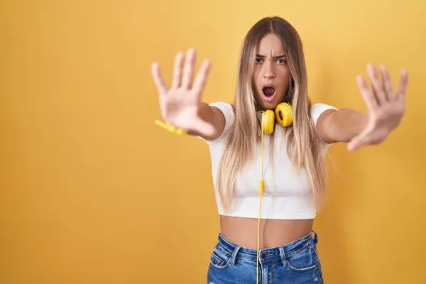 Mujer Rubia Joven Pie Sobre Fondo Amarillo Con Auriculares Haciendo —  Fotos de Stock