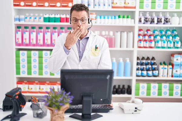 Jovem Hispânico Trabalhando Farmácia Farmácia Usando Fone Ouvido Cobrindo Boca — Fotografia de Stock