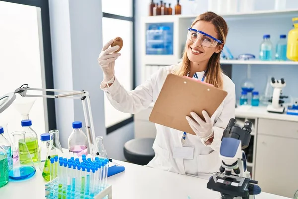 Young Blonde Woman Wearing Scientist Uniform Holding Kiwi Clipboard Laboratory — Stock Photo, Image