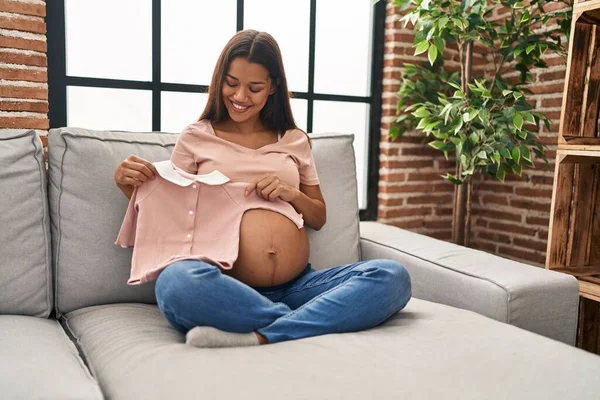 Mujer Latina Joven Embarazada Sosteniendo Ropa Bebé Casa — Foto de Stock