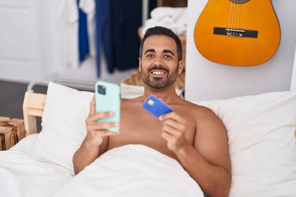 用智能手机和信用卡躺在床上躺在卧室里的年轻人 — 图库照片
