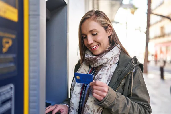 年轻的金发女人带着自信的笑容在银行出纳员面前拿着信用卡 — 图库照片