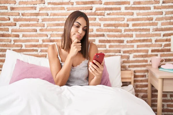 Молода Іспаномовна Жінка Використовуючи Смартфон Сидячи Ліжку Вдома Серйозне Обличчя — стокове фото