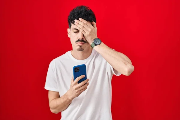 Homem Hispânico Usando Smartphone Sobre Fundo Vermelho Bocejando Cansado Cobrindo — Fotografia de Stock