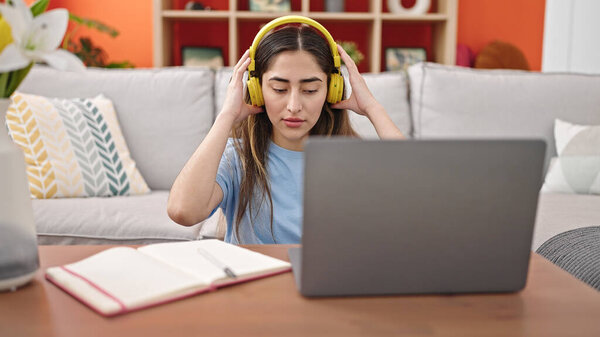 Young beautiful hispanic woman using laptop and headphones at home