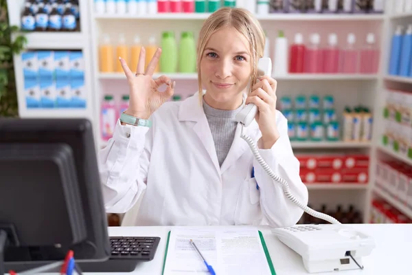 Stock image Young caucasian woman working at pharmacy drugstore speaking on the telephone smiling positive doing ok sign with hand and fingers. successful expression. 