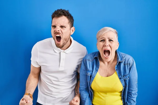 年轻的巴西母亲和儿子站在蓝色的背景上 怒气冲冲地尖叫 怒气冲冲地大叫 愤怒和好斗的概念 — 图库照片