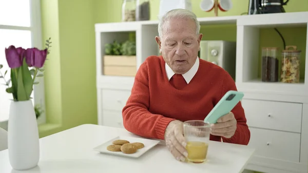 senior eating cookies and drinking juice using smartphone at home