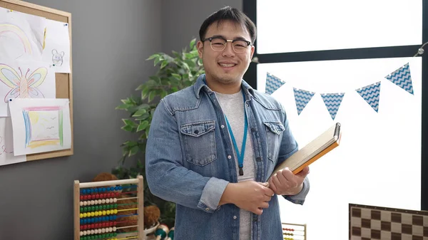 Young Chinese Man Teacher Smiling Confident Holding Books Kindergarten — Stockfoto