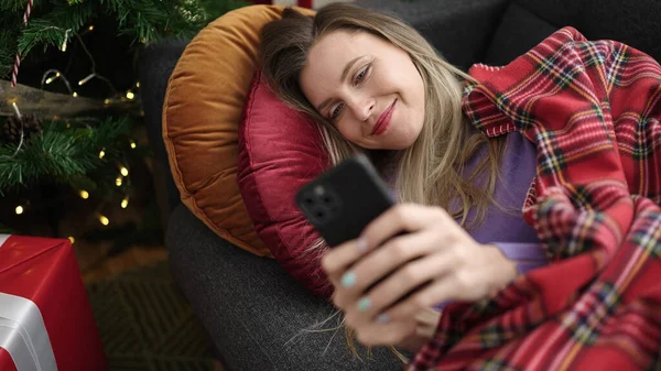 Mladá Blondýna Žena Pomocí Smartphone Ležící Pohovce Vánoční Stromeček Doma — Stock fotografie