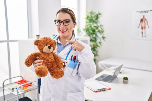 Mladá Hispánská Dětská Lékařka Drží Medvídka Klinice Šťastně Usmívá Ukazuje — Stock fotografie