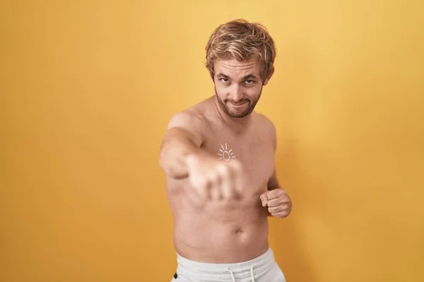 Caucasian man standing shirtless wearing sun screen punching fist to fight, aggressive and angry attack, threat and violence