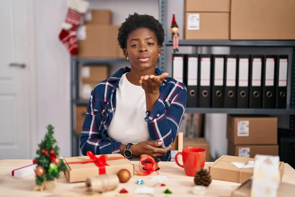 小さなビジネスで働くアフリカ系アメリカ人の女性がカメラを見てクリスマスの装飾をしていて 空気中で手でキスを吹いているのが美しくセクシーです 愛の表現 — ストック写真