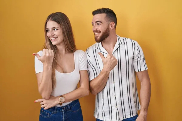 Sarı Arka Planda Duran Genç Çift Gülümsüyor Gülümsüyor Başparmağıyla Yan — Stok fotoğraf