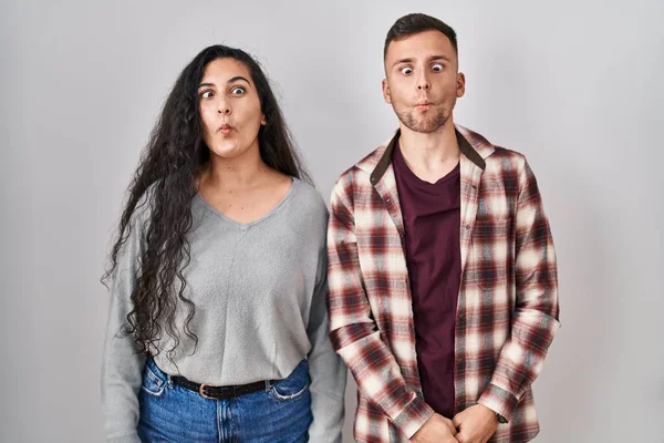 白い背景の上に立っている若いヒスパニック系のカップルは 狂気とコミカルなジェスチャーで魚の顔を作る 面白い表現 — ストック写真