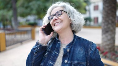 Middle age woman with grey hair speaking on the phone at park